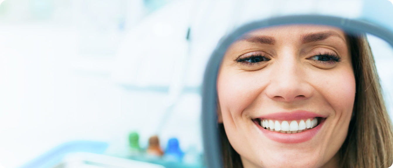 Woman smiling in dental mirror with white teeth, showing oral care results.