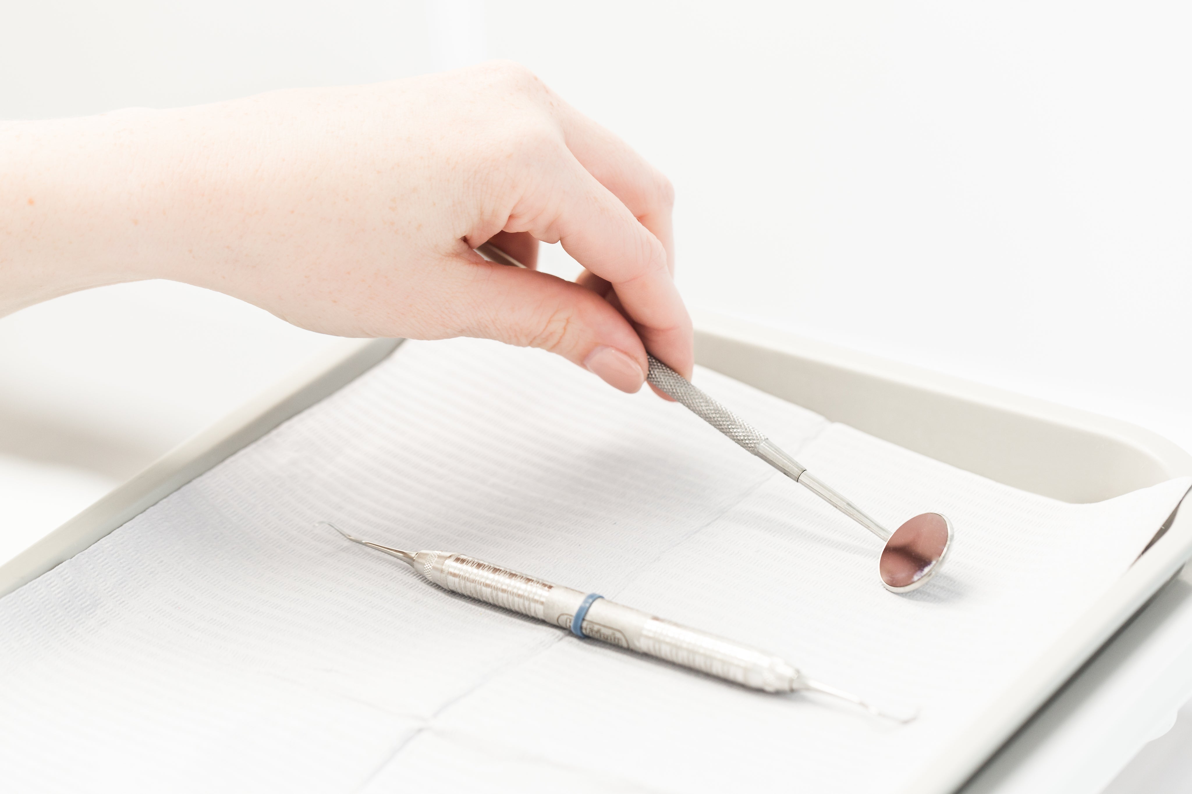 Hand picking up dental mirror tool from tray, used for teeth and oral care.