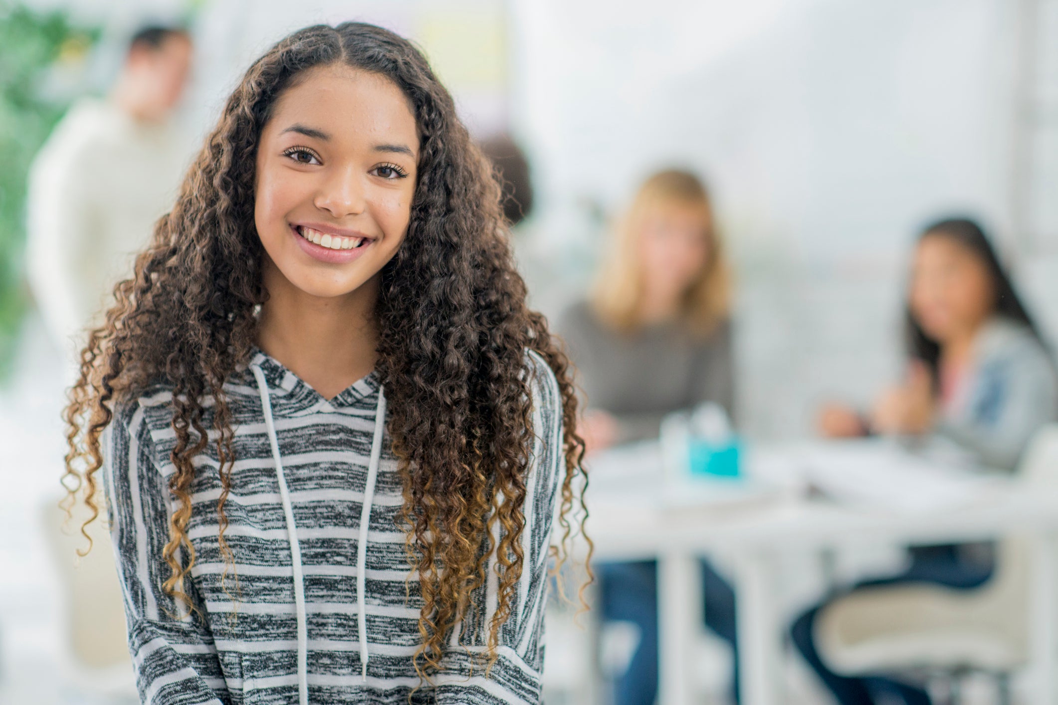 Smiling teen with healthy teeth in a classroom setting, emphasizing youth dental and oral care.